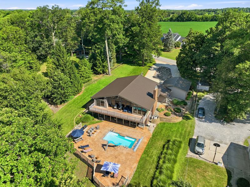Overhead drone view of a wooded lakeside home with a deck and in-ground pool
