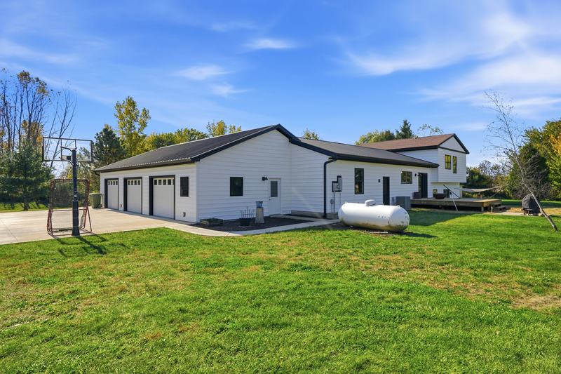 Modern white farmhouse with a dark roof under a bright blue sky