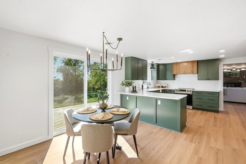 Dining area with a modern chandelier opening onto a green-cabinet kitchen