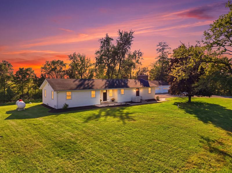 Ranch home with warmly lit windows beneath a vivid orange and violet sunset sky